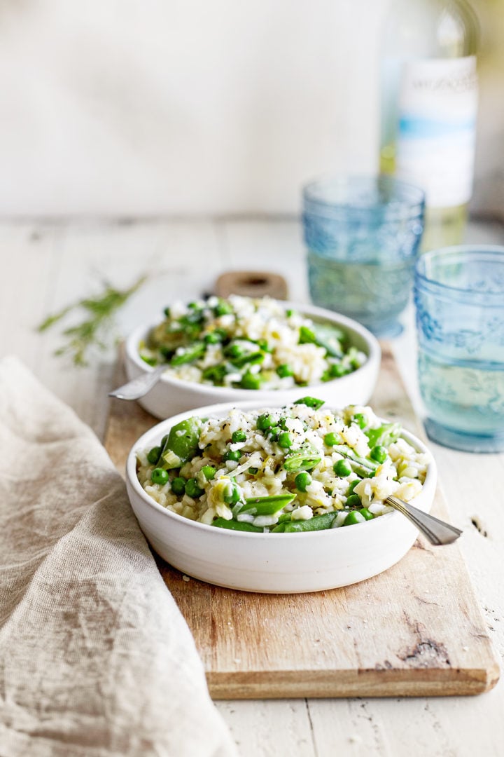 two bowls of spring risotto next to glasses of wine