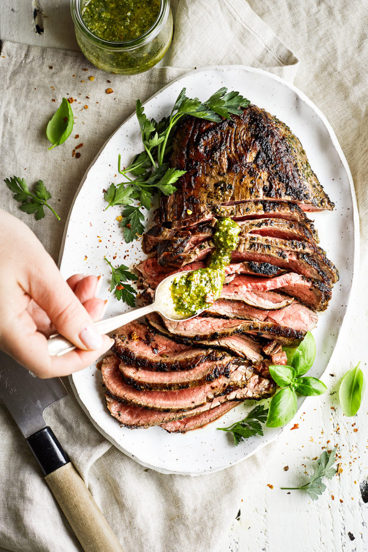 woman drizzling chimichurri sauce on top of grilled chimichurri skirt steak
