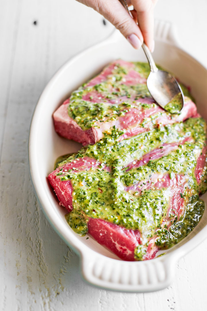 woman spooning chimichurri skirt steak marinade on meat in a dish