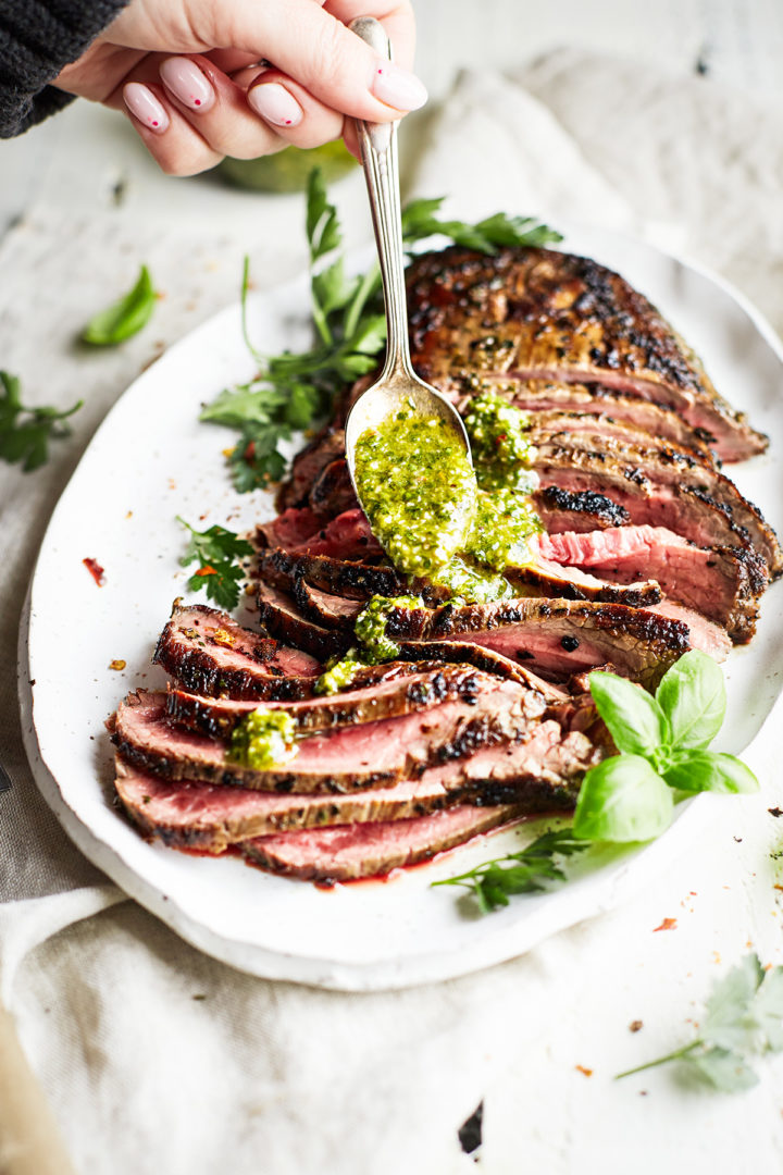 woman drizzling chimichurri sauce on  grilled skirt steak
