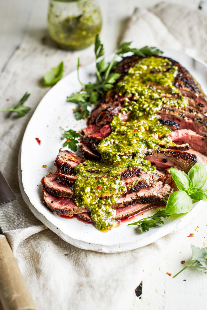 sliced chimichurri skirt steak on a white platter with chimichurri sauce