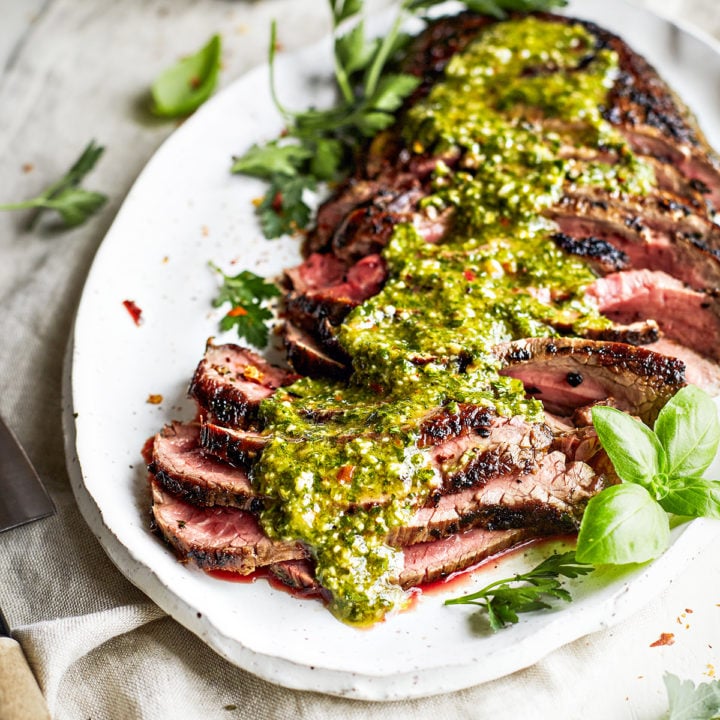 sliced chimichurri skirt steak on a white platter with chimichurri sauce