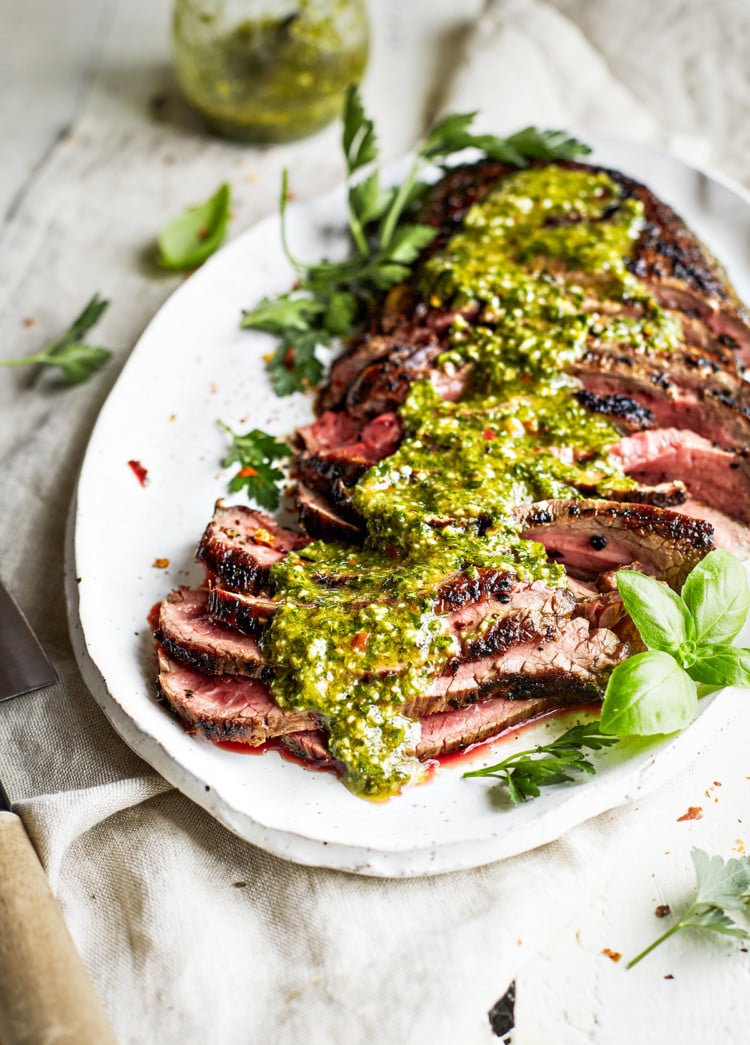 sliced chimichurri skirt steak on a white platter with chimichurri sauce