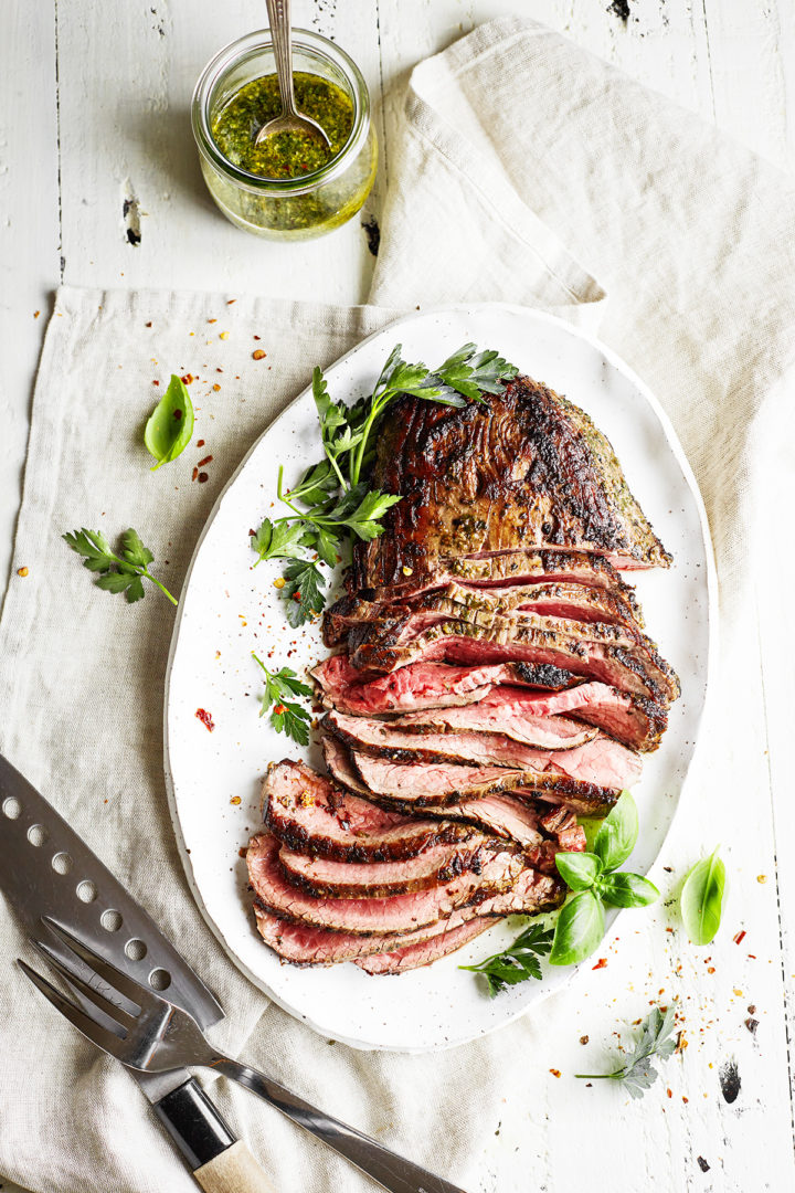 a platter of grilled skirt steak with chimichurri sauce in a jar