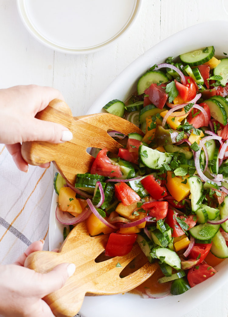 woman serving a cucumber tomato onion salad