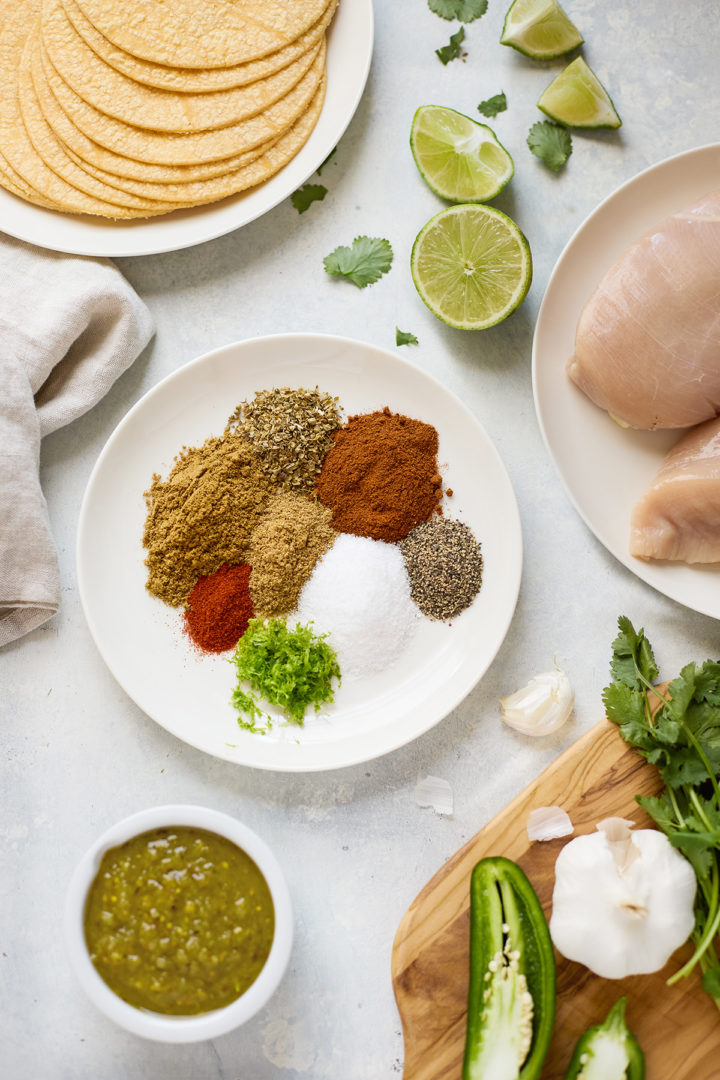 Overhead view of fresh ingredients for Instant Pot shredded chicken tacos, including spices, salsa, and boneless chicken breasts.