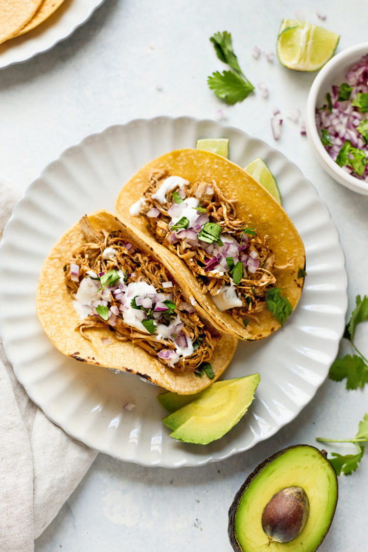 Fully assembled Instant Pot chicken tacos on a plate, topped with avocado, cilantro, and red onion—easy, flavorful, and family-friendly.