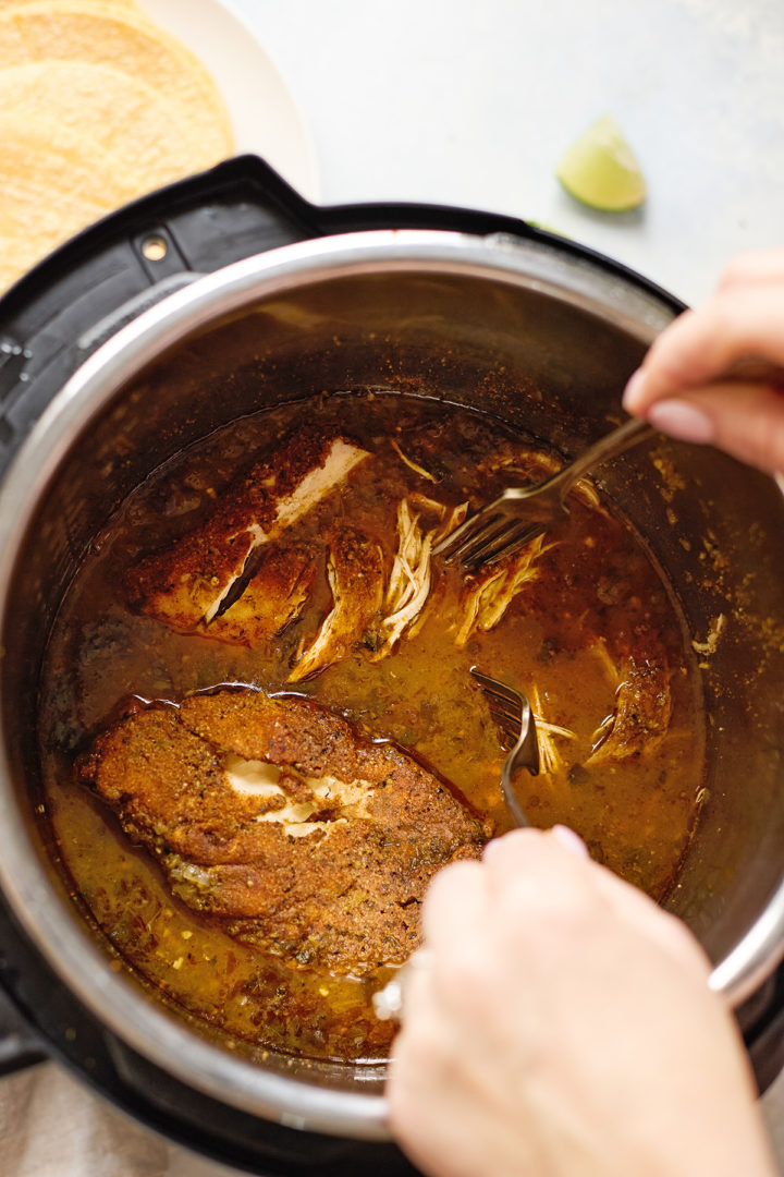 Close-up of a woman shredding juicy chicken taco meat in the Instant Pot—perfect for quick Instant Pot shredded chicken tacos or meal prep.