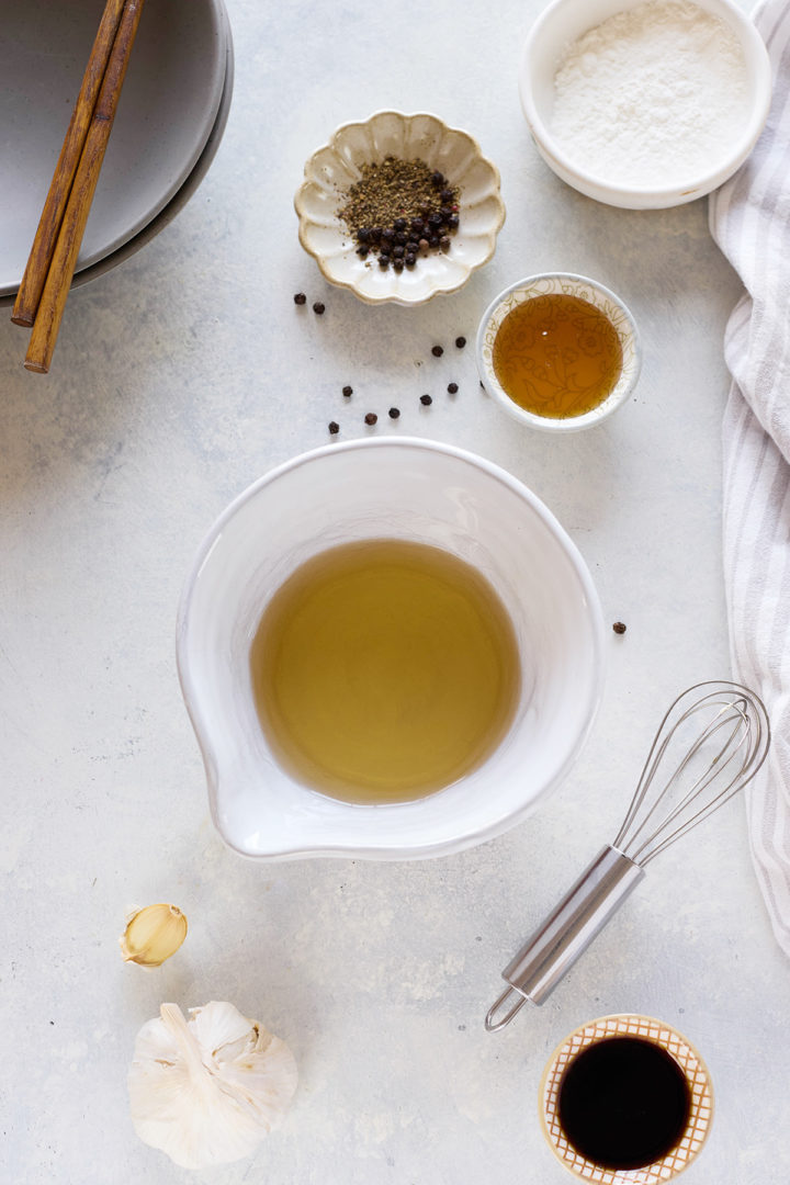 Overhead view showing small white bowls filled with ingredients for the black pepper sauce, including coconut aminos, dry sherry, coarsely ground black pepper, and minced garlic and ginger, all arranged on a dark slate surface.