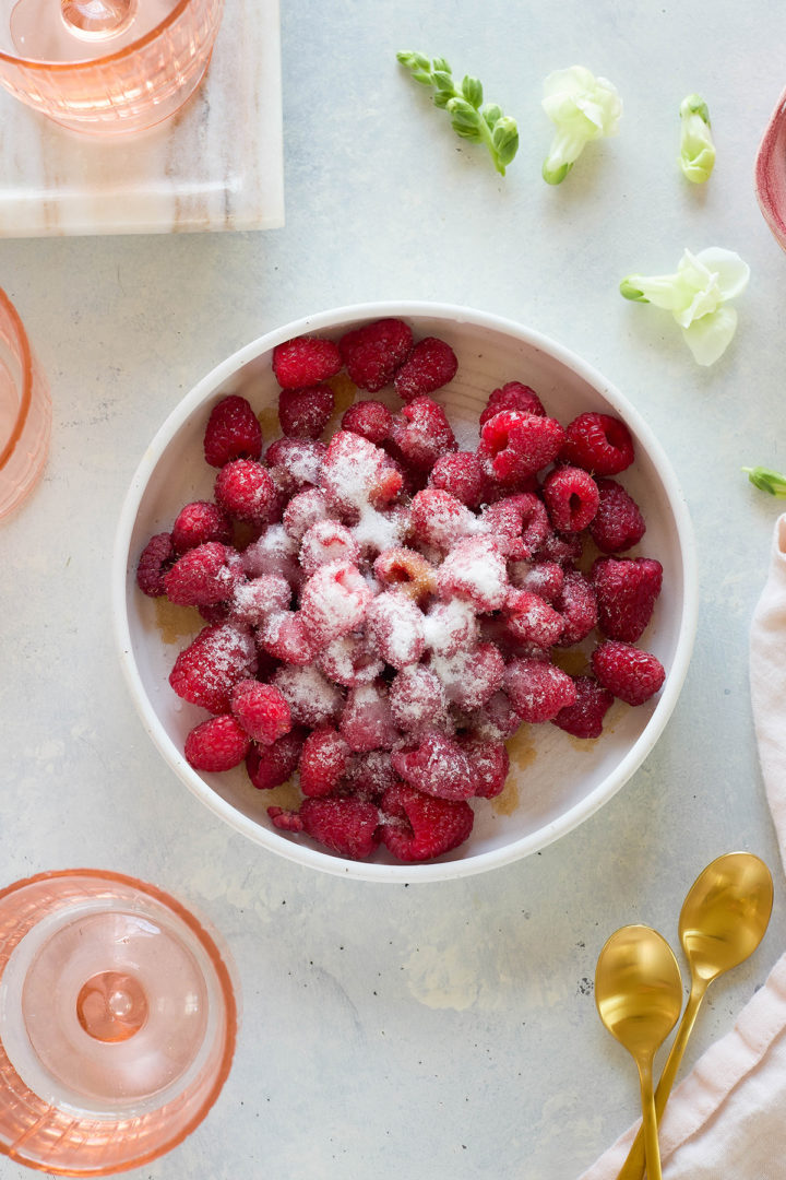 Bowl of fresh raspberries coated with sugar, prepared for mashing to make the raspberry layer in an easy raspberry fool recipe.
