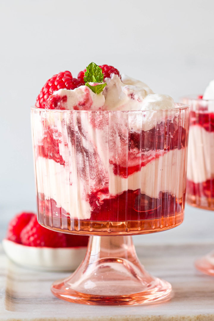 Glass dessert cup filled with raspberry fool, showing distinct layers of raspberries and whipped cream, garnished with a raspberry and mint sprig.