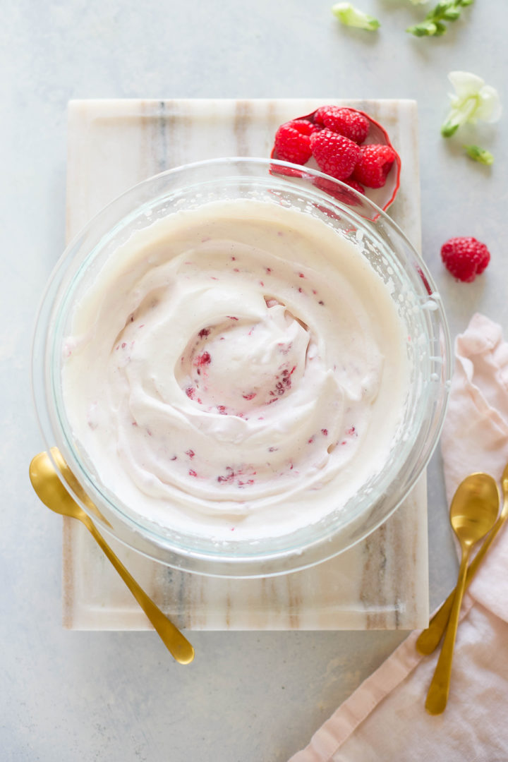Glass bowl filled with whipped cream mixed with raspberry puree, part of the process of making raspberry fool from scratch.