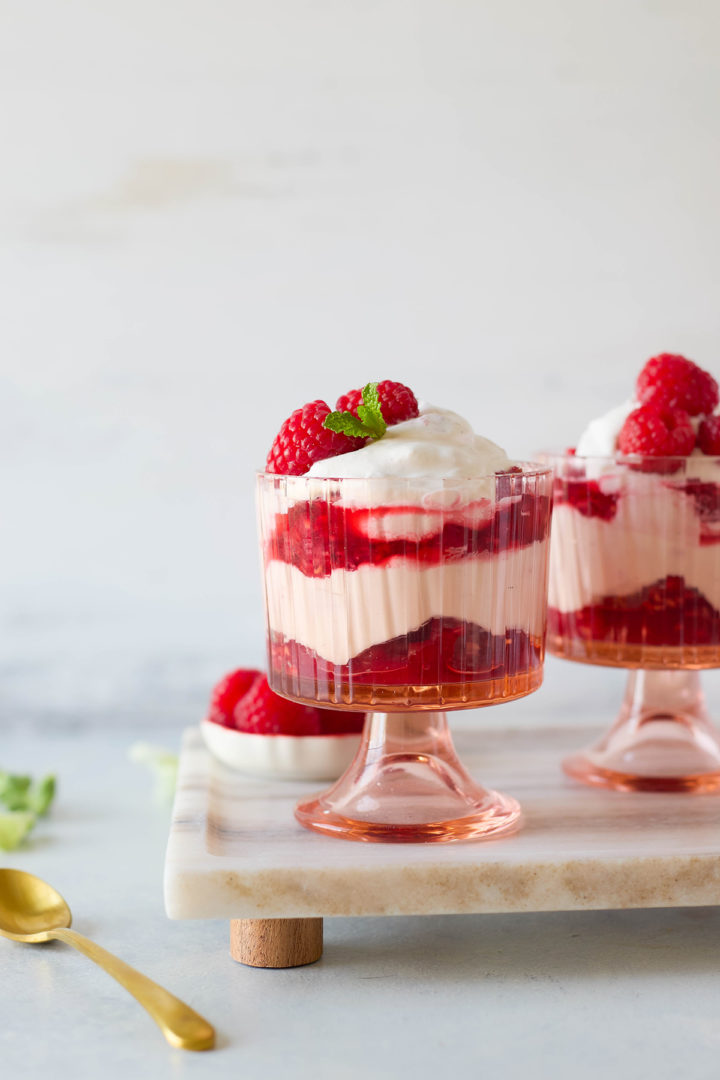 Raspberry fool served in glass cups with layers of whipped cream and raspberry sauce, topped with raspberries and mint on a marble tray.