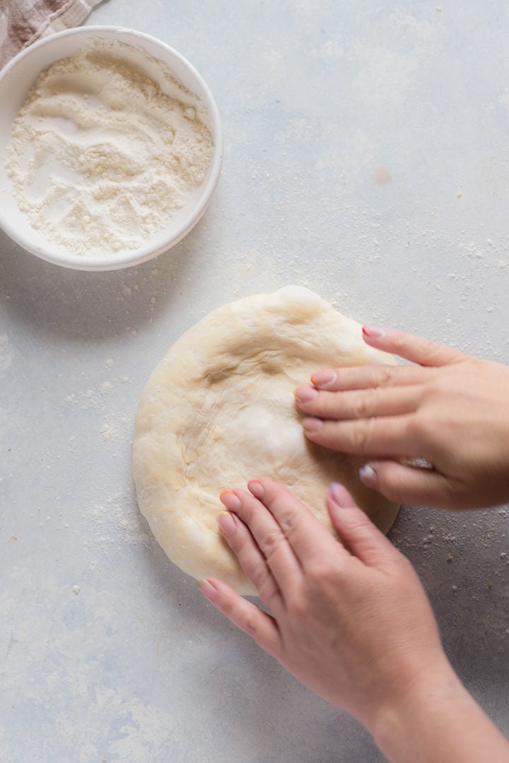 Hands gently pressing and stretching pizza dough on a floured countertop, preparing it for toppings.