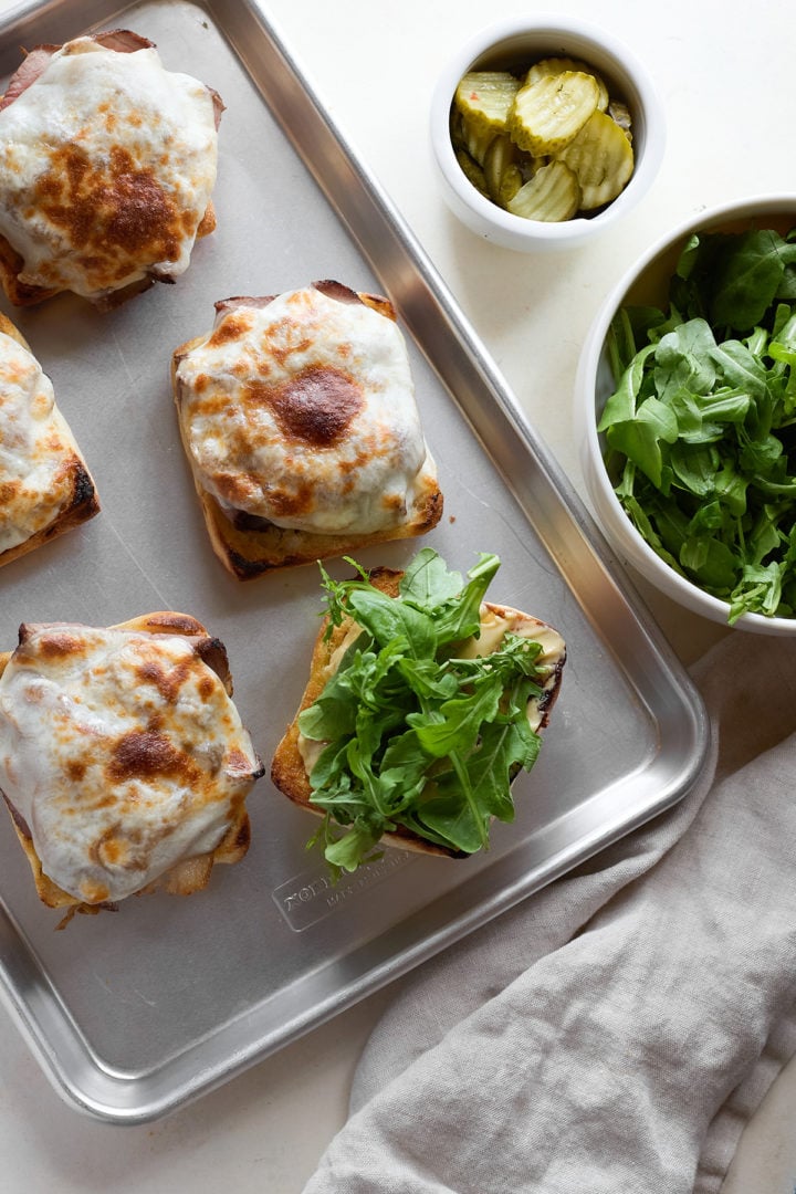 One sandwich base is topped with a pile of fresh arugula, while the others remain with their melted provolone tops.
