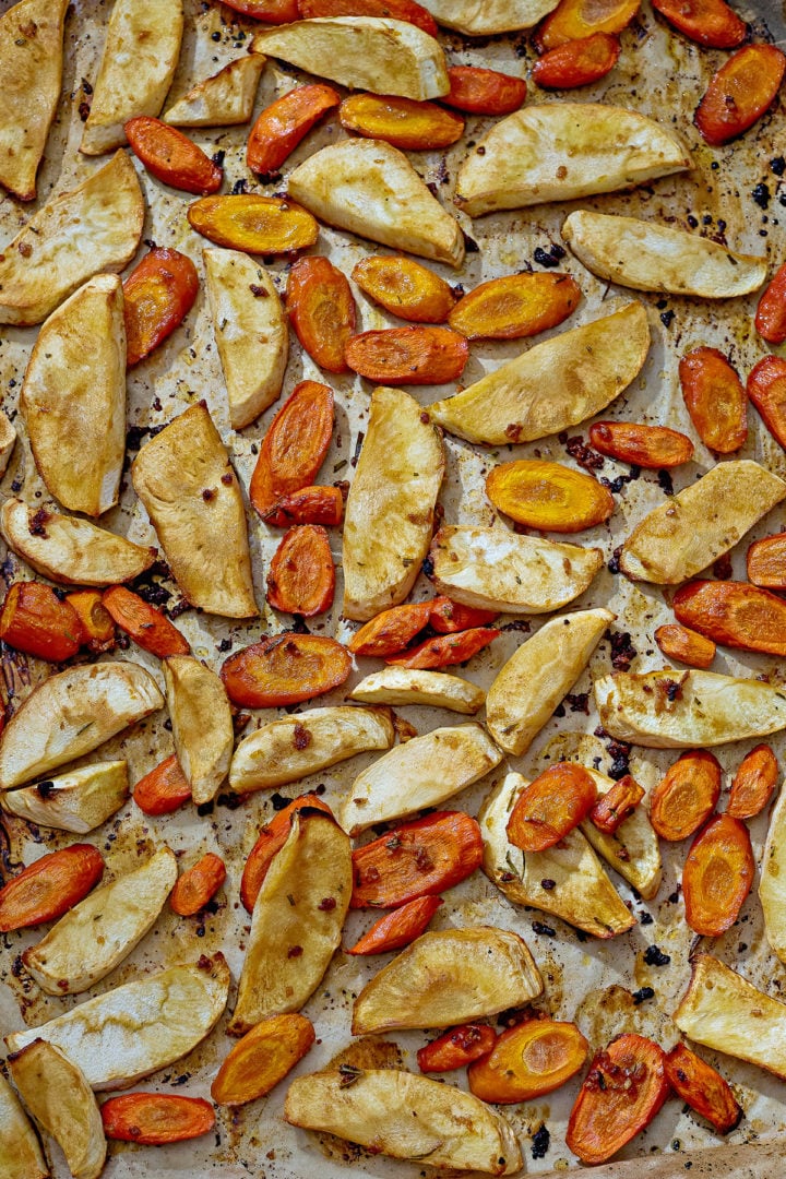 Roasted parsnips and carrots on a  baking sheet, caramelized and golden from honey and olive oil.