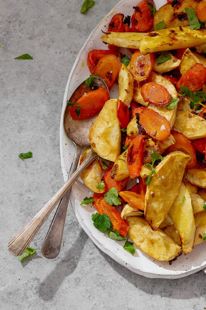 Closeup of caramelized roasted parsnips and carrots with golden edges and fresh parsley.