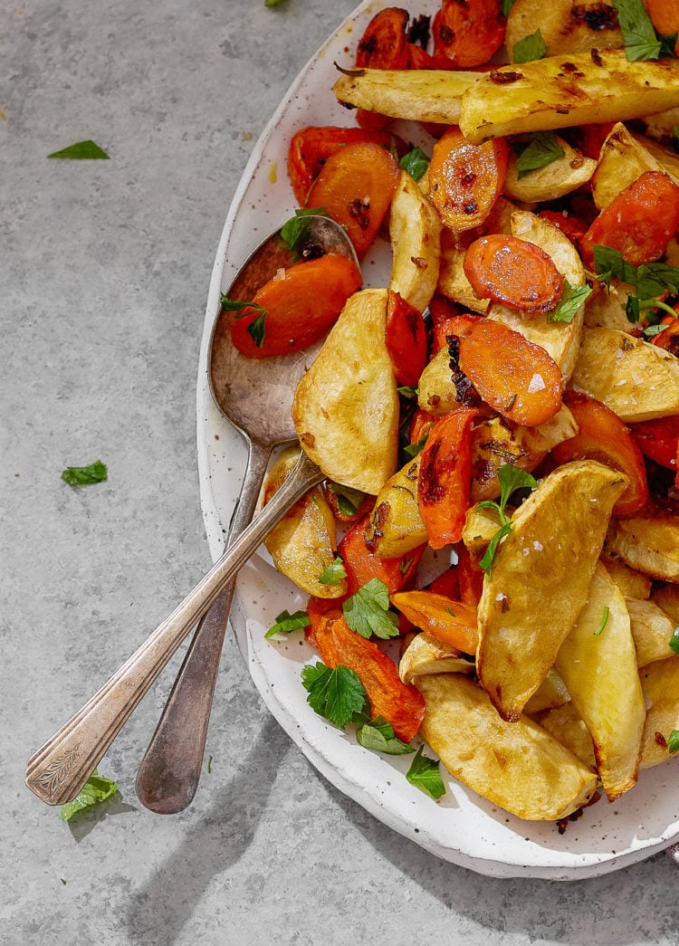 Closeup of caramelized roasted parsnips and carrots with golden edges and fresh parsley.