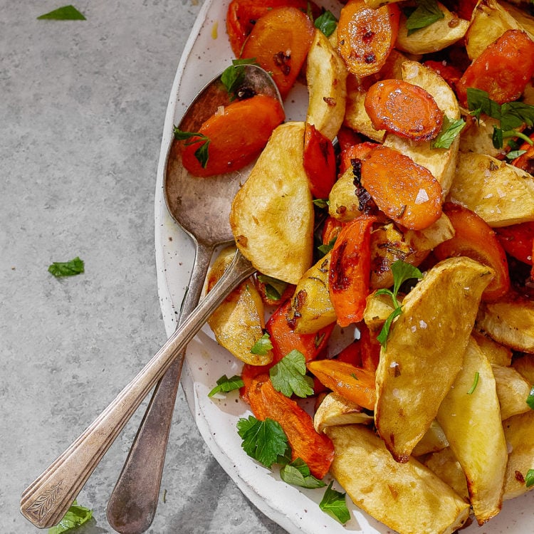 Closeup of caramelized roasted parsnips and carrots with golden edges and fresh parsley.