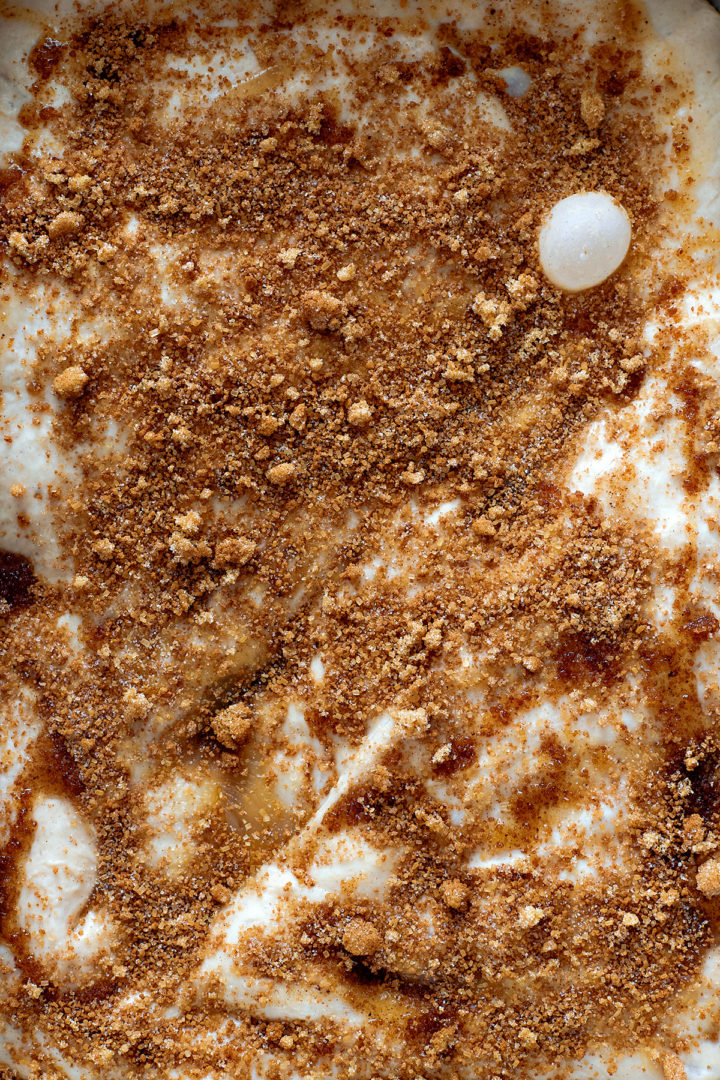 Close-up overhead view of raw focaccia dough covered with melted butter, brown sugar, and cinnamon scattered unevenly across the surface before baking.