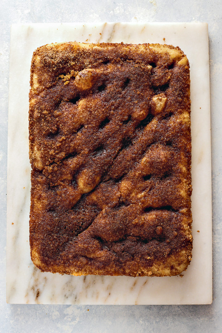 Overhead view of a full, uncut cinnamon sugar focaccia fresh out of the oven. The surface is golden brown and bubbled, with dark swirls of caramelized cinnamon sugar across the top.